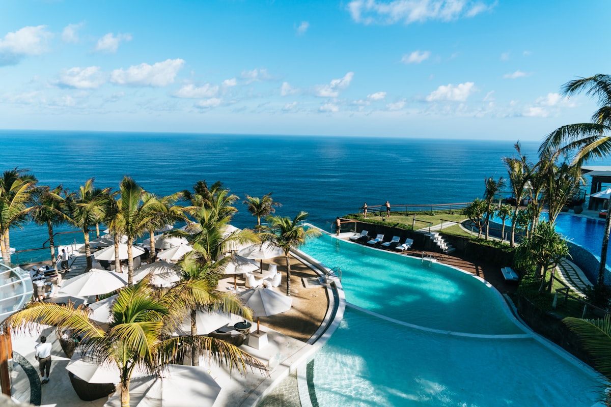 Stunning infinity pool at a luxury tropical resort overlooking crystal clear turquoise ocean, lush palm trees, pristine white sand beach, bright sunny day, cinematic aerial photography, no people